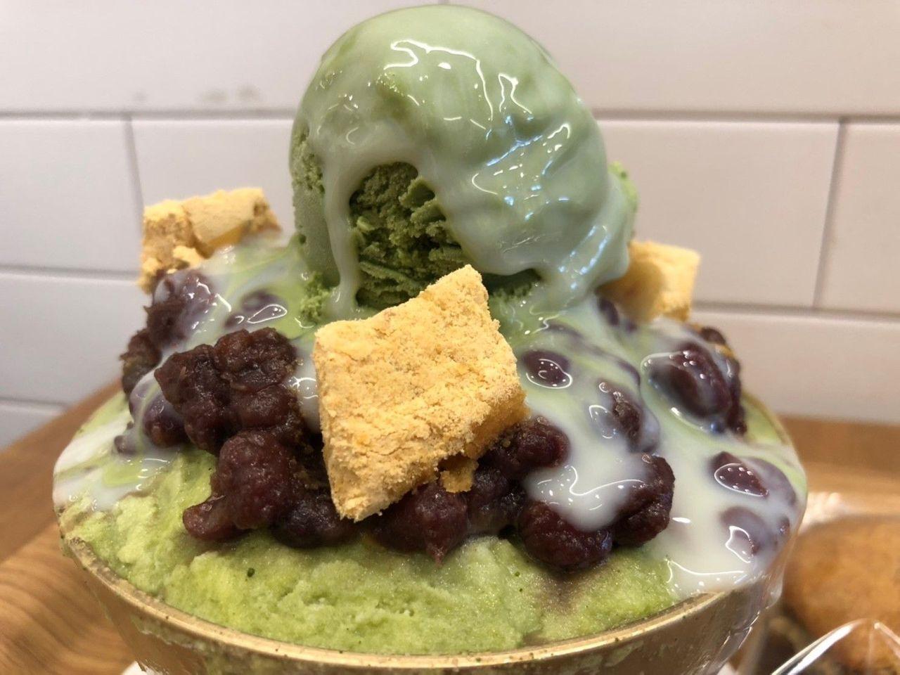 篱笆边的菊花咖啡厅经典绿茶刨冰特写，顶部淋上香浓的炼乳，浓郁红豆点缀于其上，甜美诱人。